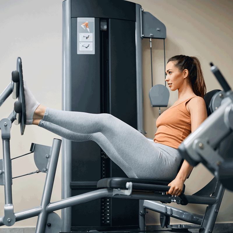 Young female athlete exercises on leg press machine in health club.